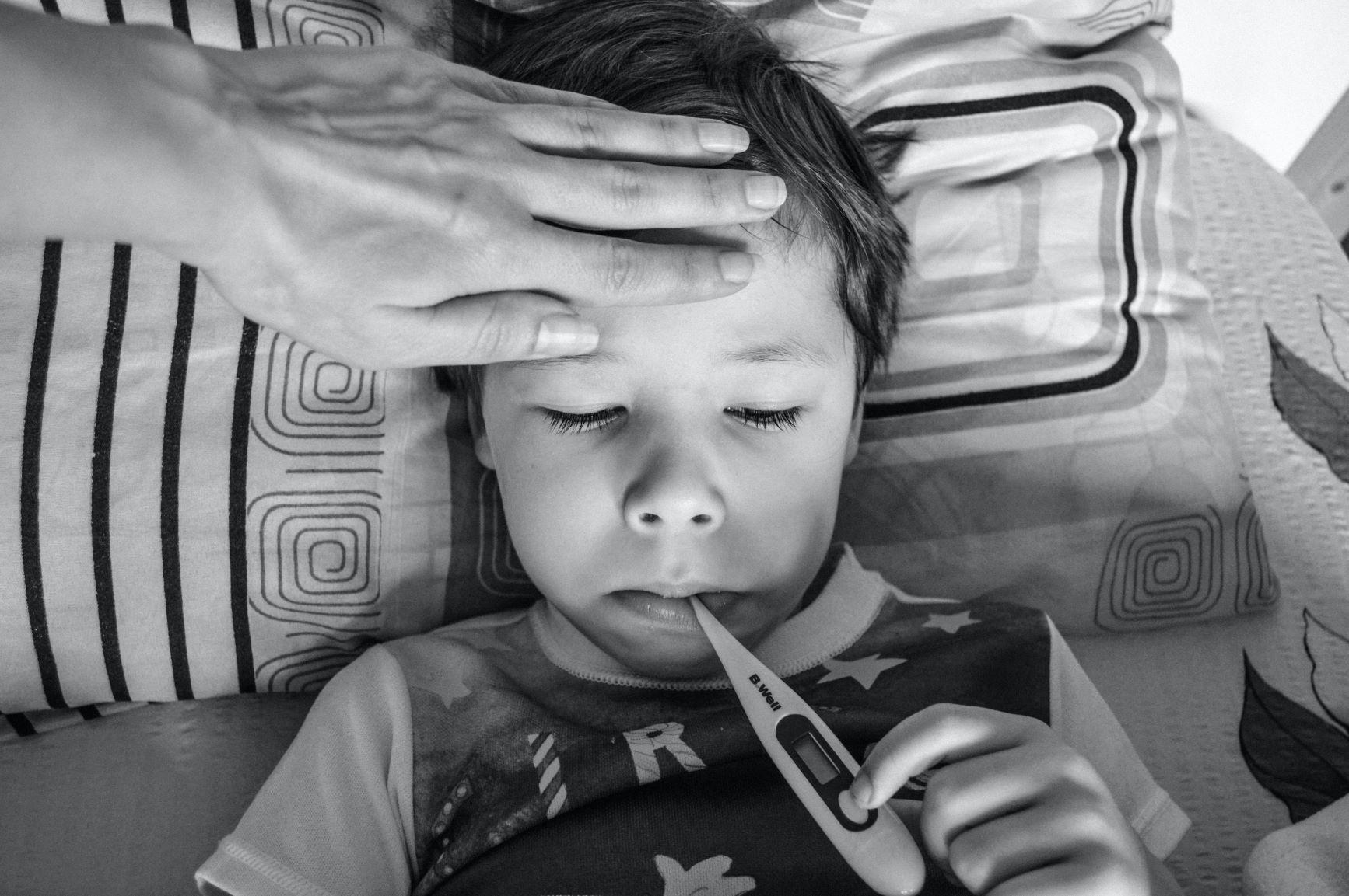 Kind im Bett mit Fieberthermometer